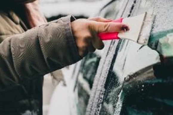Person entfernt Eis von Autoscheibe